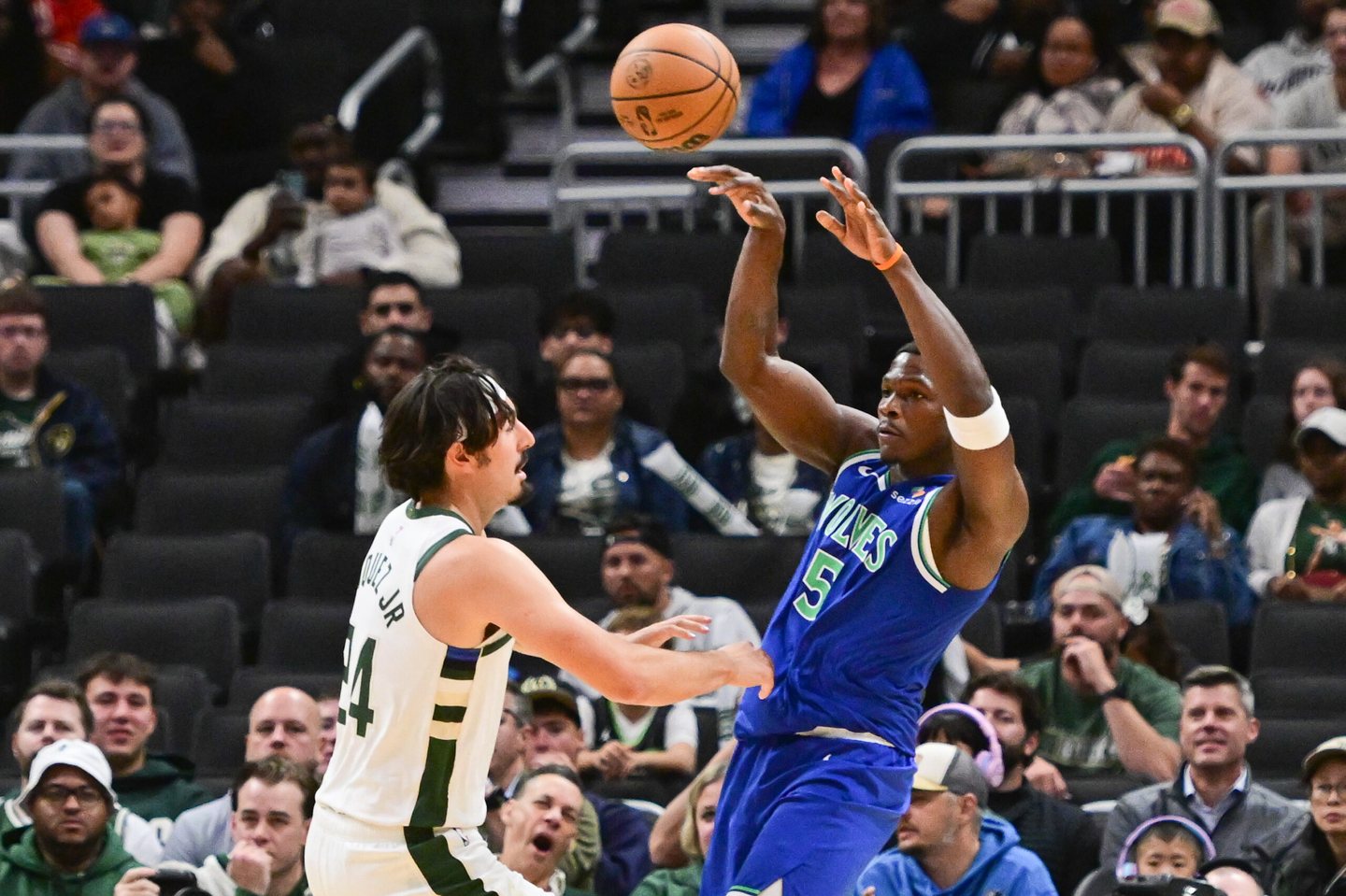 Anthony Edwards in a blue Timberwolves jersey passes over Milwaukee forward Jaime Jaquez Jr. in the first quarter.
