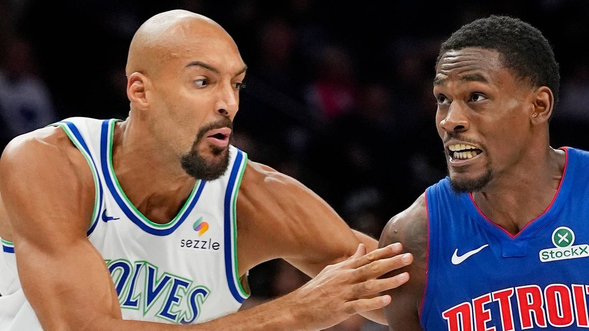 Rudy Gobert, in a white Timberwolves jersey, defends a Detroit Pistons player in a blue jersey.