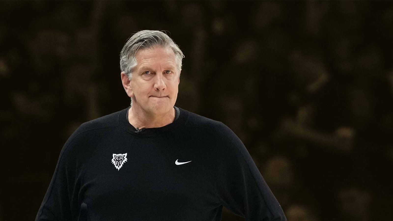 Chris Finch in a black Timberwolves pullover looks on, lips pressed.