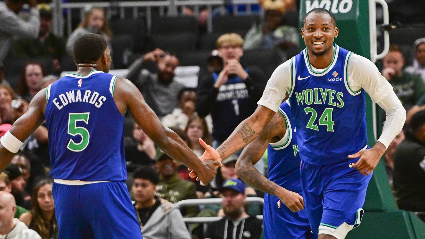 Jonathan Kuminga and Anthony Edwards reach toward each other in blue Wolves uniforms in Milwaukee.